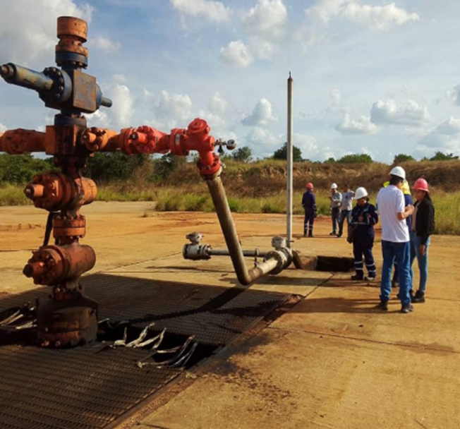 Árbol de navidad y tuberías en campo petrolero con personal con EPP